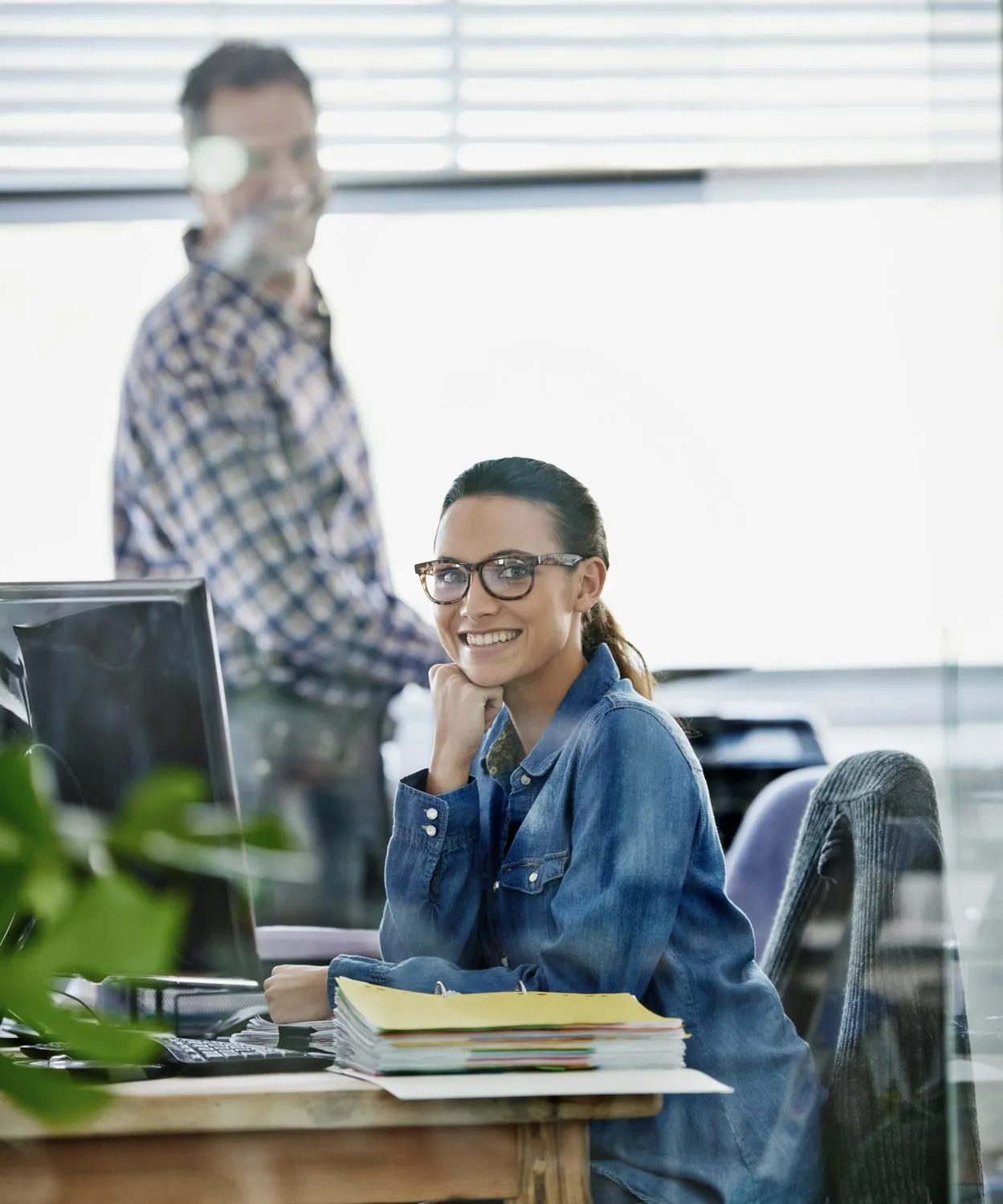 A smiling woman at her office desk with a coworker