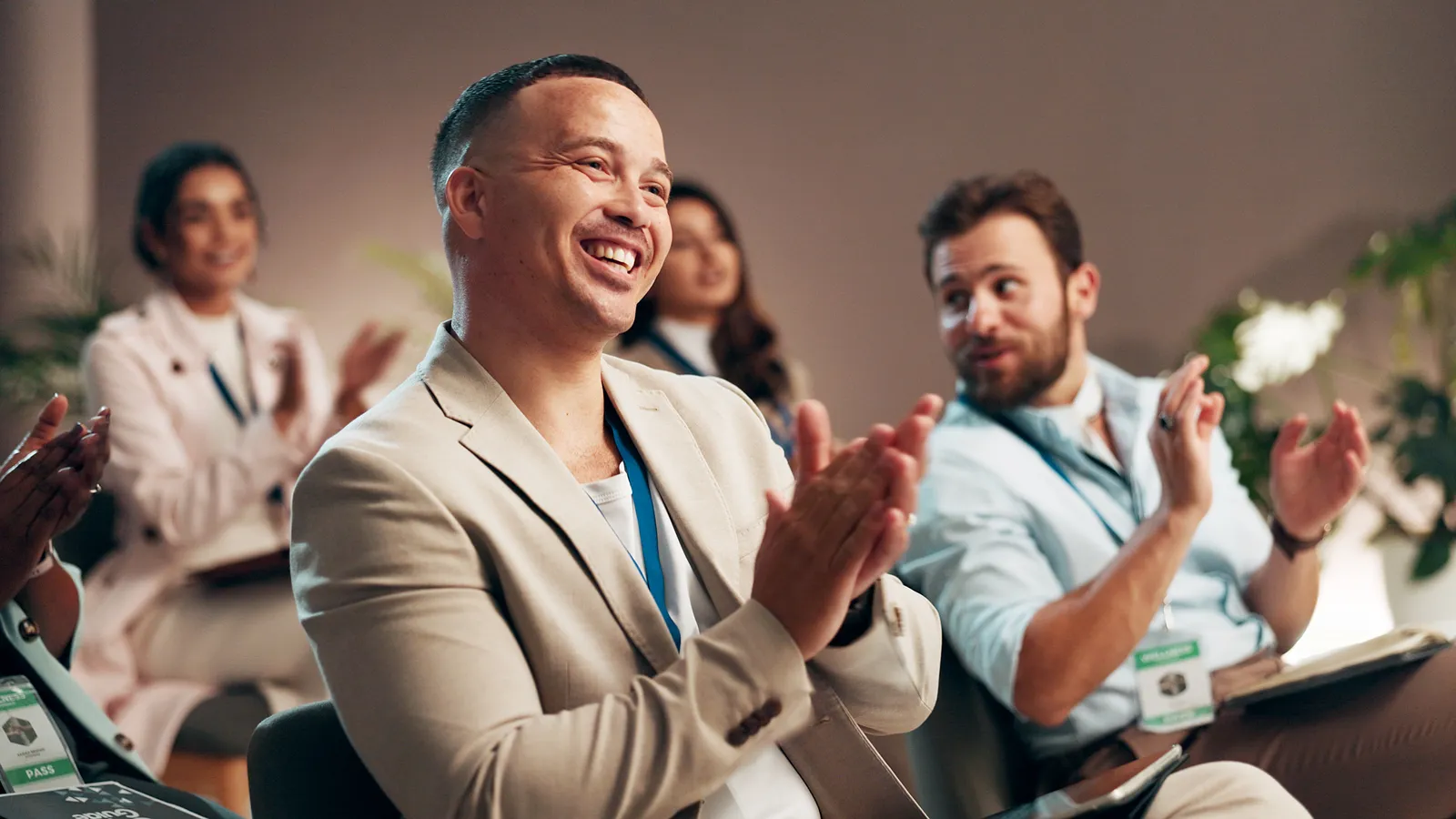 Smiling business people with conference passes applauding from the audience.